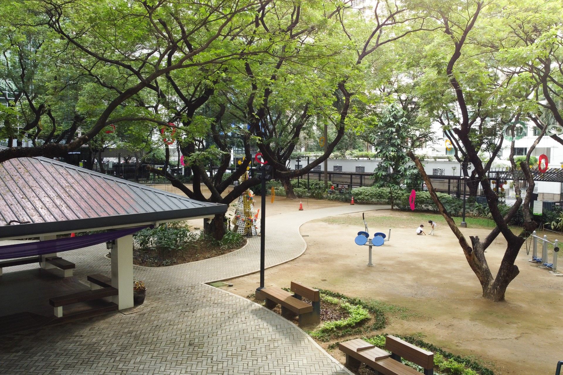 A village park with a pavilion, paths, benches and exercise equipment under the trees