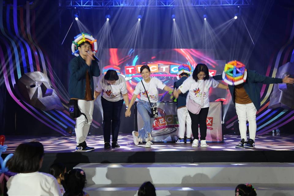Performers on a brightly lit stage at night, children watching from the front